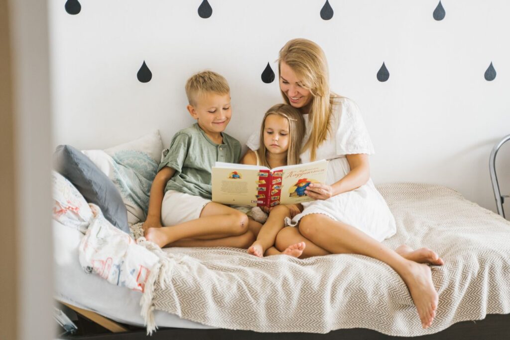 Home A mother and her two children enjoy a cozy reading session together on a bed.