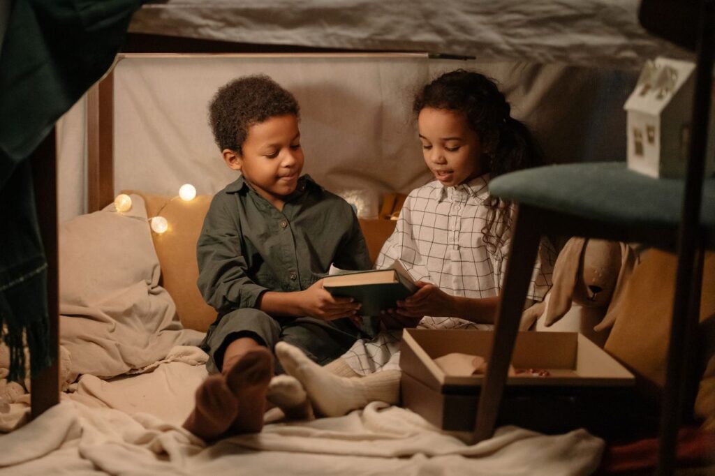 Two children sharing a book in a warm and playful indoor tent setting, fostering sibling bonding.