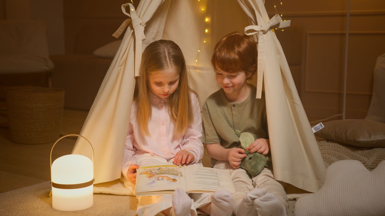 Hello world! Two children reading a book inside a cozy tent indoors, creating a warm and friendly atmosphere.